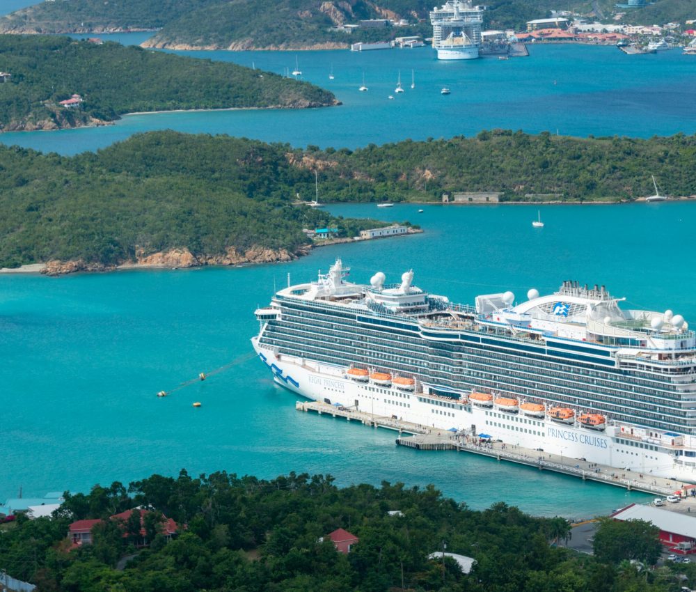 Aerial view of a luxury cruise ship docked in a turquoise Caribbean harbor on a sunny day.